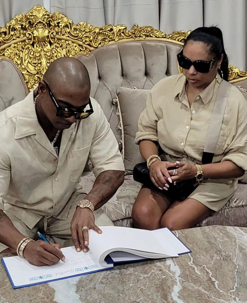 Ja Rule signing a document with a woman seated beside him.